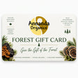 A Forest Gift Card from Annanda Organics featuring a cream background with green and gold branding, pine and mushroom illustrations, and the text 'Give the Gift of the Forest'.